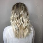 A woman with long blonde hair is standing in front of a wall.
