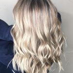 A woman with long blonde hair is standing.