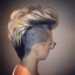 A woman with short hair and glasses in front of a wall.