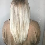 A woman with long blonde hair is standing in front of a wall.