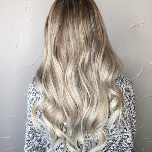 A woman with long blonde hair is standing in front of a wall.