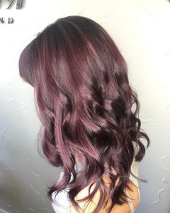 A woman with long, dark hair is wearing a purple wig.